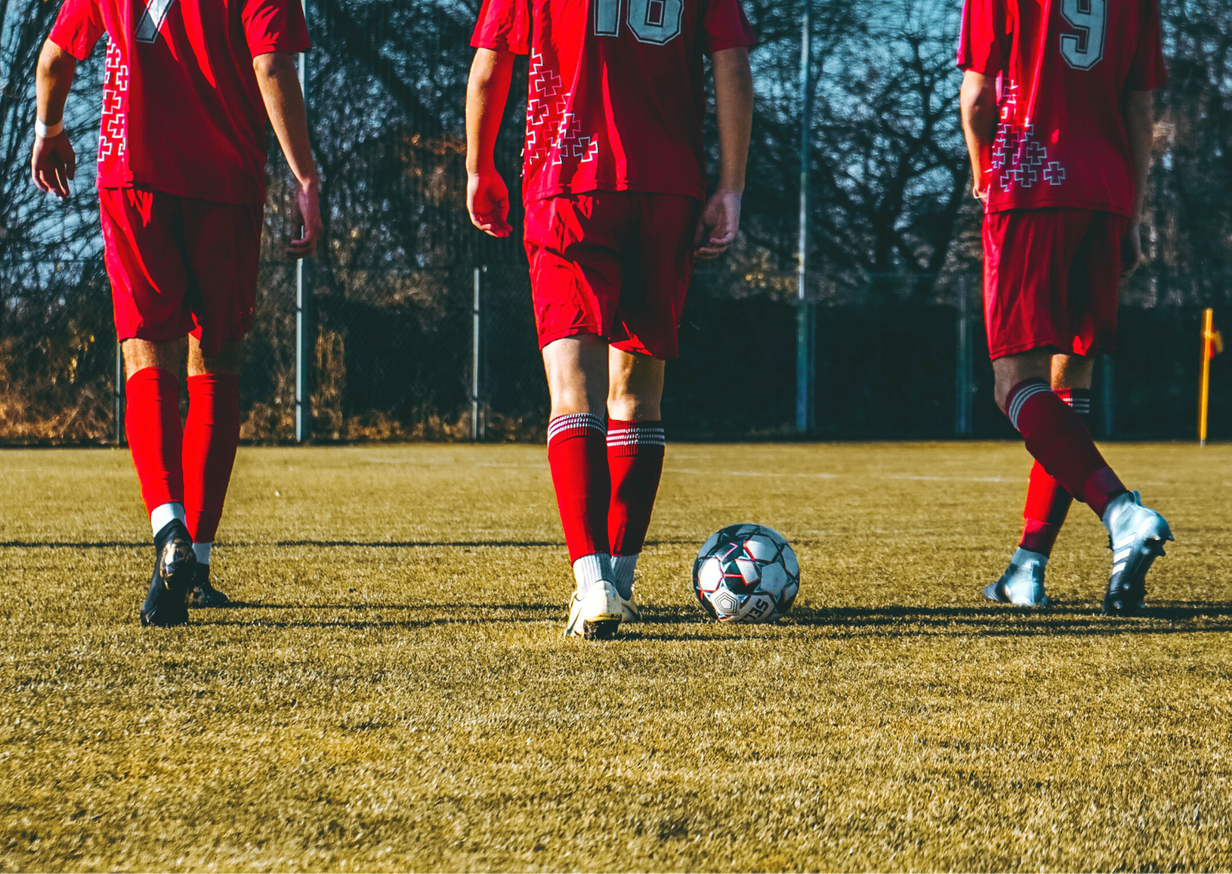 Tre mænd i rødt på en fodboldbane med en fodbold
